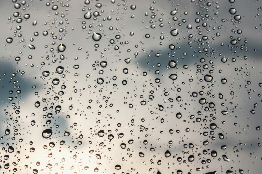 Wassertropfen aus Kondensation auf einer Glasscheibe vor grauem Hintergrund